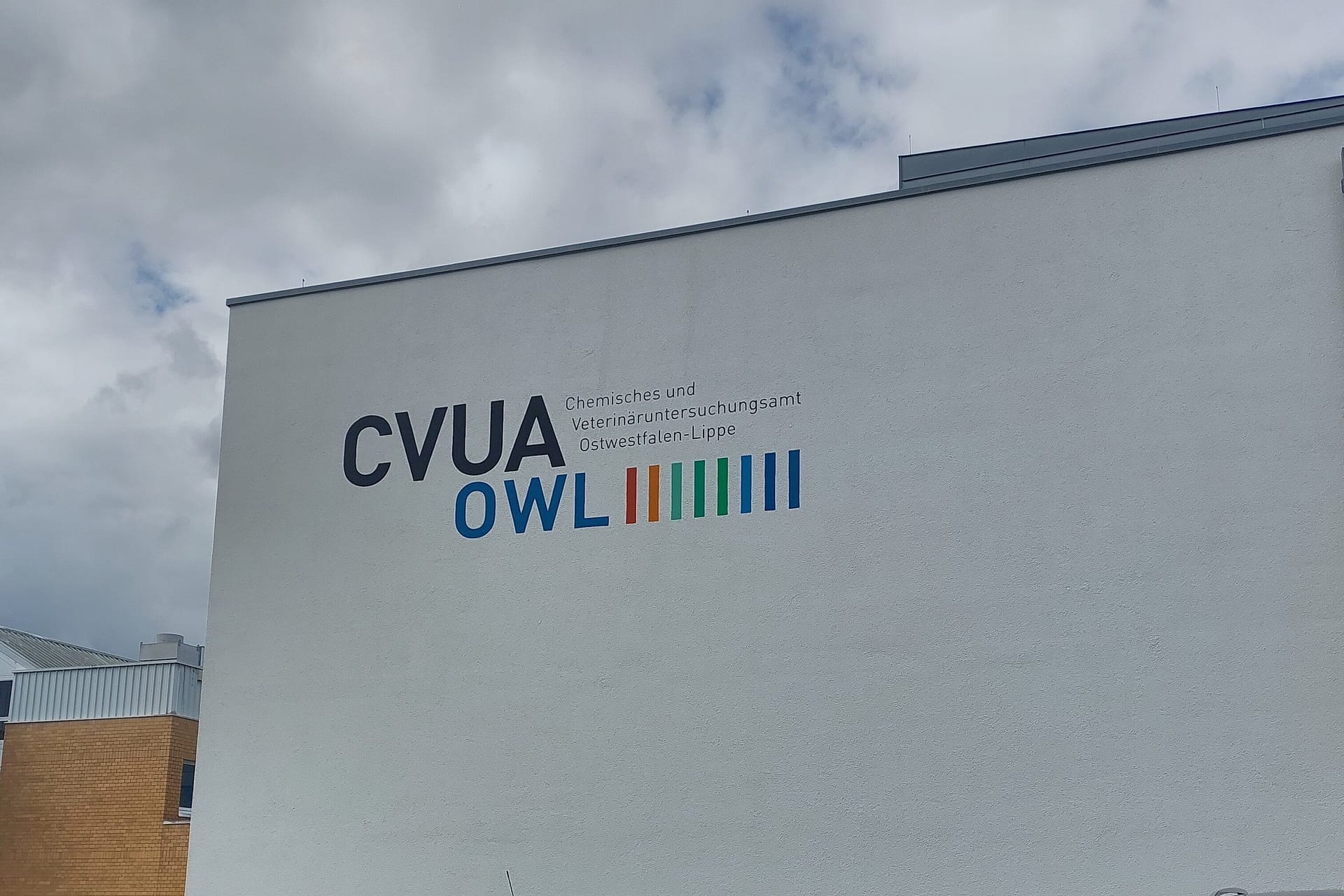 Detektive im weißen Kittel: Was das CVUA Detmold für unseren Honig leistet 12 Außenansicht des Dienstgebäudes des CVUA OWL in Detmold mit Parkplatz, einem markanten türkisfarbenen Opel Corsa B mit Bielefelder Kennzeichen und dem CVUA-Logo an der Fassade.